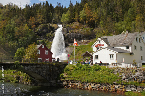 Steinsdalsfossen waterfall in the river of Steine - scenic landscape with cascade surounded by mountains and traditional norvegian, scandinavian houses