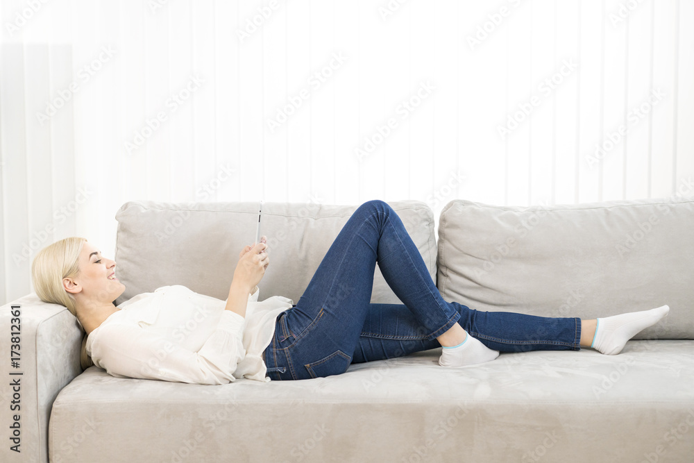 The happy woman lay on the sofa and hold a tablet The happy woman lay on the sofa and hold a tablet