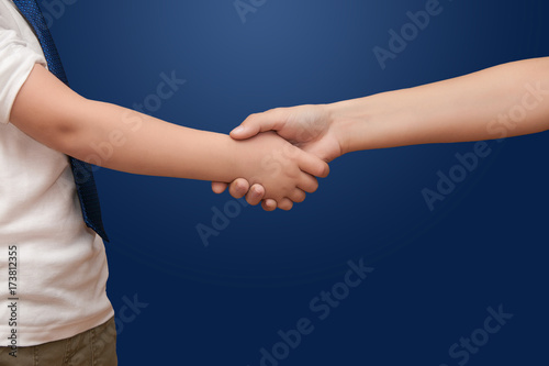 child's hand shakes hands with a teenager on a blue background