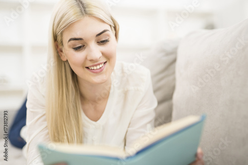 The happy woman lay on the sofa and reading the book