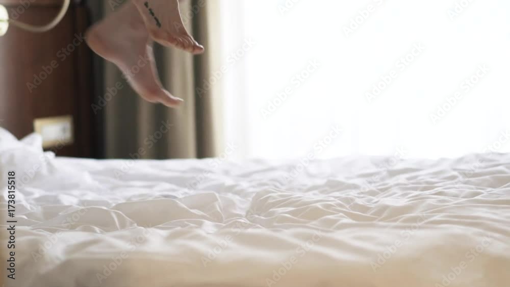 Side view of legs of a young woman who is jumping on her king size bed with white bedding. Locked down slow motion close up shot Side view of legs of a young woman who is jumping on her king size bed with white bedding. Locked down slow motion close up shot