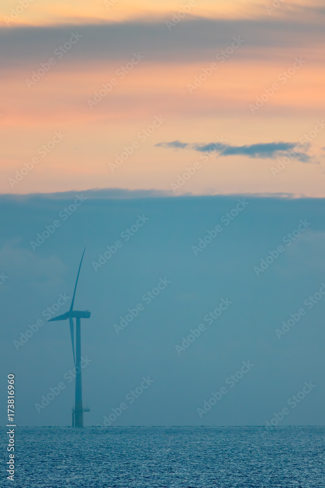 Clean energy. Soft image of misty morning pastel sky over calm sea with offshore wind turbine
