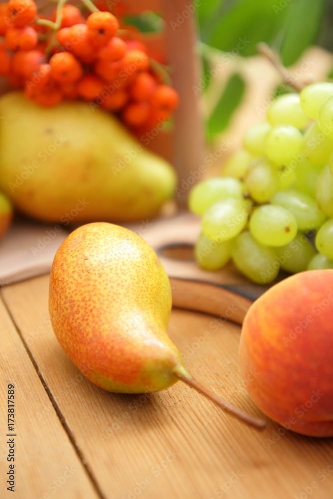 Pears, peach, green grapes, rowan berries in a wooden box on a wooden table in the woods at the time of harvesting Pears, peach, green grapes, rowan berries in a wooden box on a wooden table in the woods at the time of harvesting