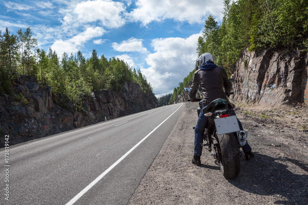 Motorbike driver is ready to start moving on the asphalt route, sitting on motorbike on roadside, rear view Motorbike driver is ready to start moving on the asphalt route, sitting on motorbike on roadside, rear view