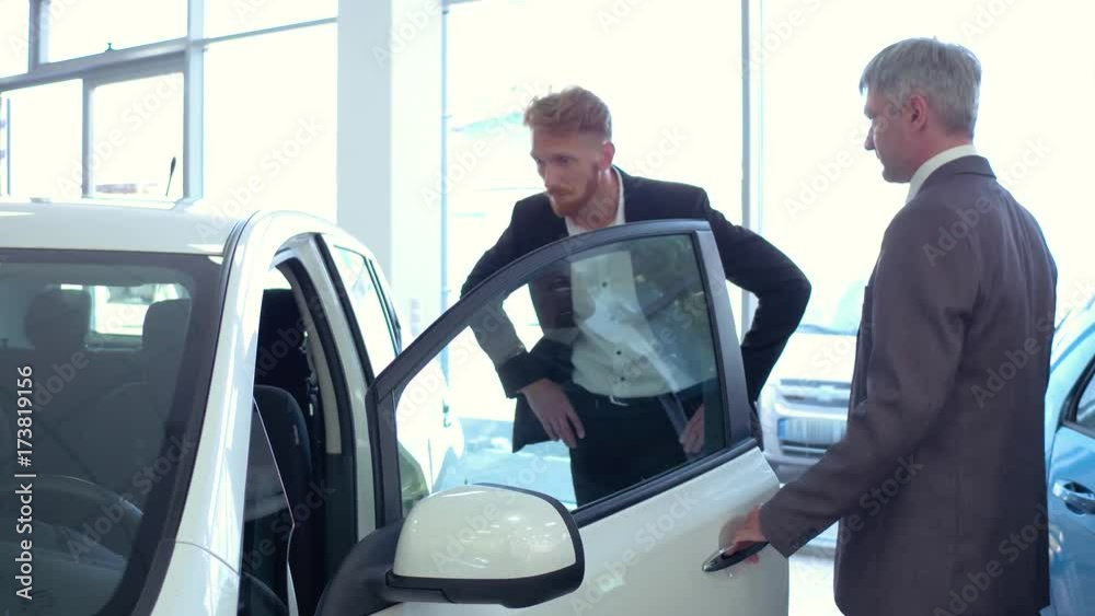 Auto showroom, sales manager showing new car to young man. Vehicle dealer and byuer inspecting car interior. Auto showroom, sales manager showing new car to young man. Vehicle dealer and byuer inspecting car interior.