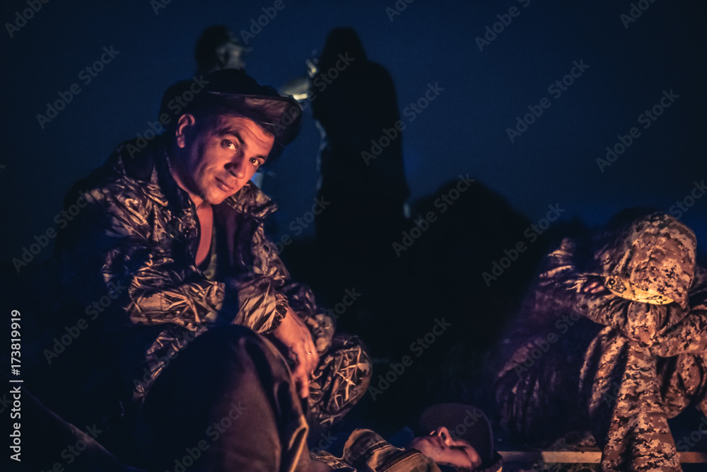 Father and son sitting by the fire in outdoors camp in the night  after long hunting day