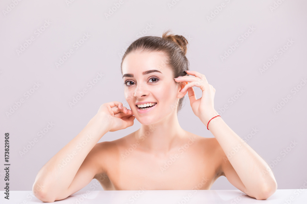 Young attractive girl with black hair fixed behind, big eyes, thick eyebrows and naked shoulders holding hand near face at gray background, portrait, copy space. Young attractive girl with black hair fixed behind, big eyes, thick eyebrows and naked shoulders holding hand near face at gray background, portrait, copy space.