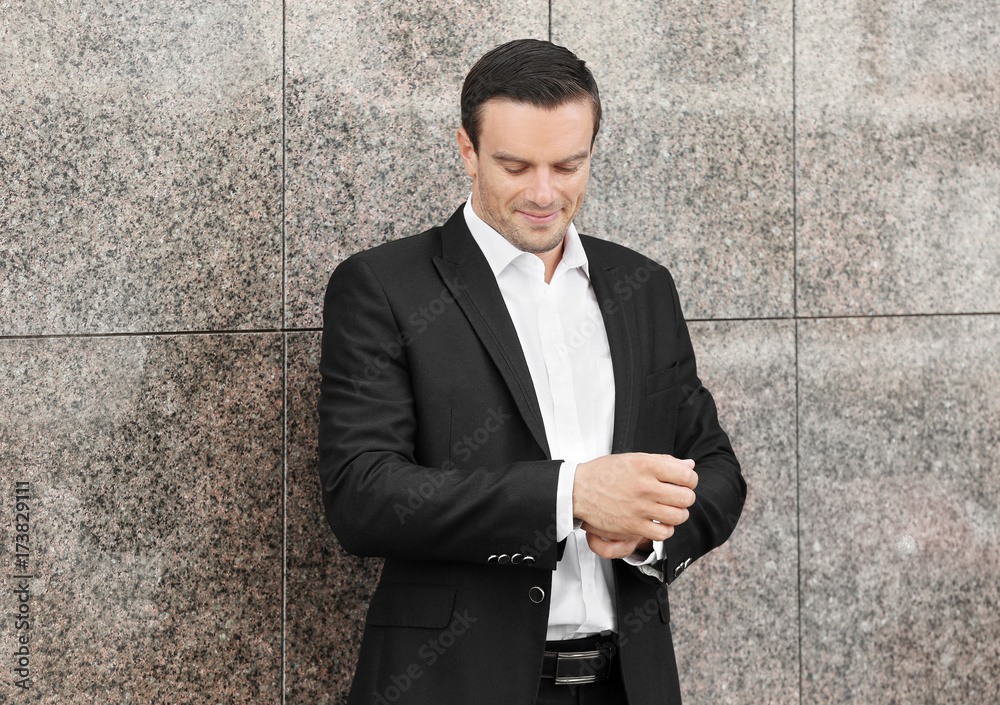 Handsome man in elegant black suit standing near wall outdoors Handsome man in elegant black suit standing near wall outdoors