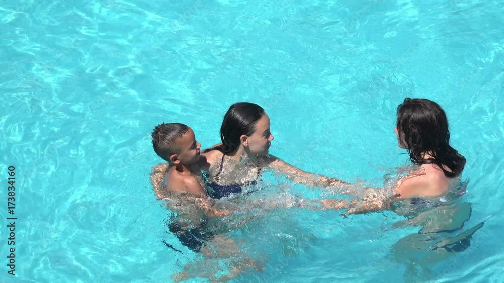 Happy family playing splashing in blue water of swimming pool 