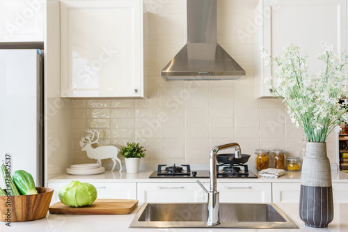 Counter top made in ceramic seen closely with fruits and vegetable on a brown color clay dish next to the modern silver faucet attached to the sink, the silver refrigerator .