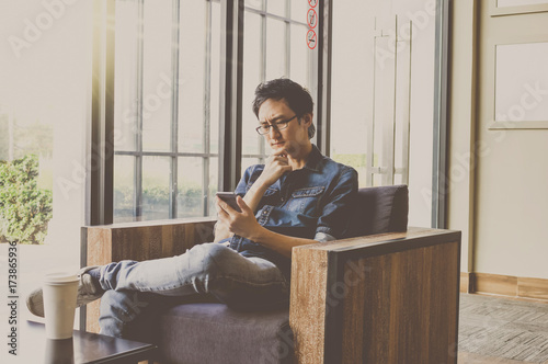 Happy asian businessman sitting on working space and using the smart mobile phone with serious action in the modern Office or coffee shop. business technology concept