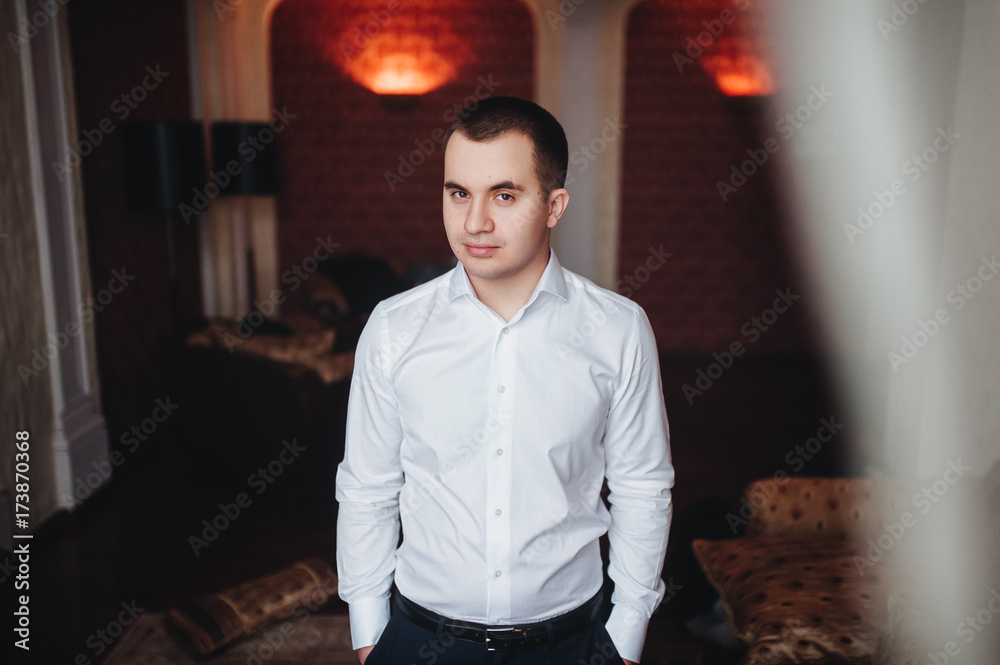 Fototapeta premium A handsome confident young man standing seriously in a white shirt in house.