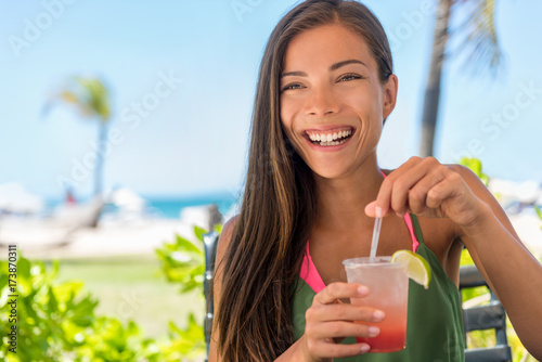 Beach vacation woman drinking cocktail having fun at hotel resort bar. Laughing Asian girl with fruit juice at outdoor terrace on tropical Caribbean holidays.