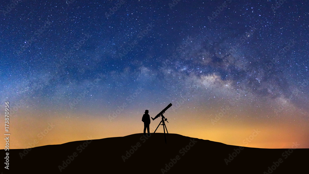 Silhouette of a standing man with telescope watching the wilky way galaxy