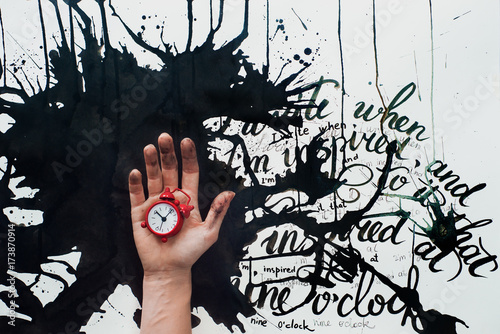 Hand holding a tiny red alarm clok on a background with spilled ink and an inspirational quote. Creative flat lay with writer workplace. Conceprual still life with copy space. photo