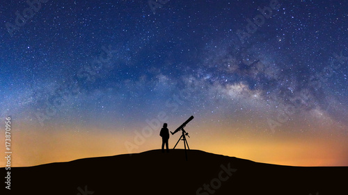 Silhouette of a standing man with telescope watching the wilky way galaxy