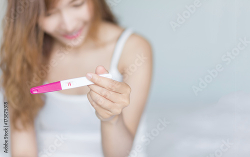 Selective focus Pregnancy test positive result on hand of smiling woman in her bedroom,Blurred background.