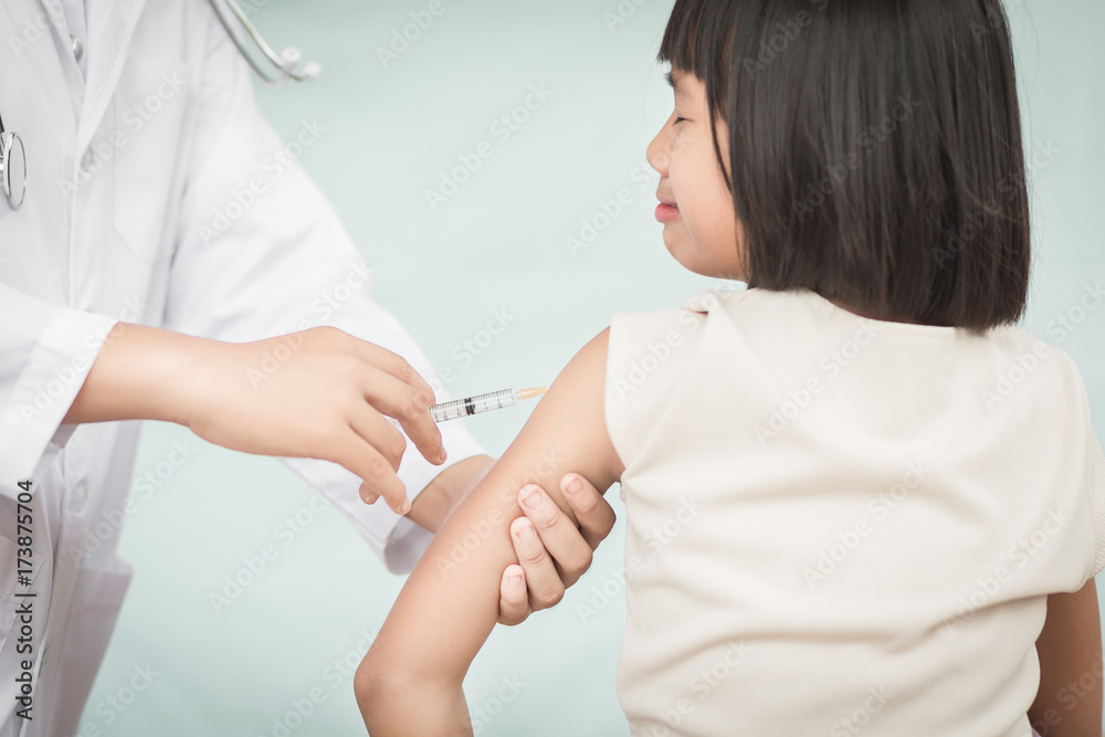 © chompoo - Doctor holding a syringe with a liquid inside next to a girl arm. © chompoo - Doctor holding a syringe with a liquid inside next to a girl arm.