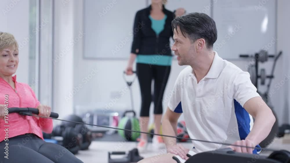 Mature woman working out on rowing machine with personal trainer Mature woman working out on rowing machine with personal trainer