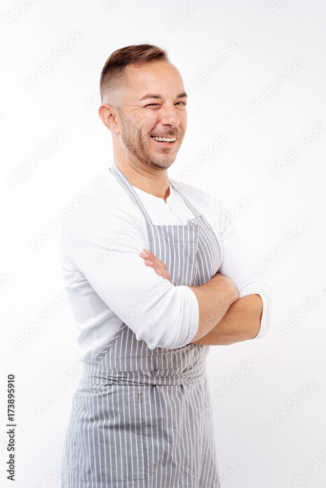 Cheerful man in apron folding arms and winking Cheerful man in apron folding arms and winking