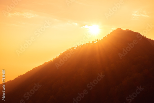 Sunset scene on hight mountain. Sunshine through the clouds. silhouette at the mountain.