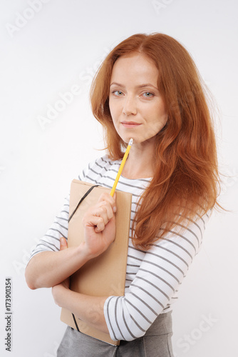 Red-haired woman touching chin with tip of pencil
