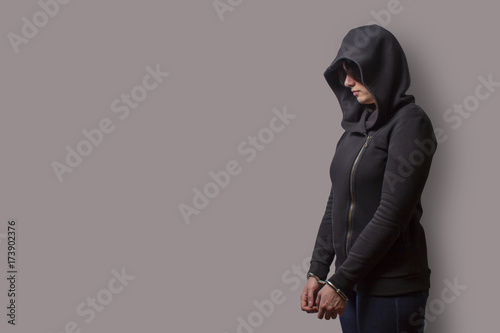 side view of a girl in a black hood with handcuffed hands isolated on a gray