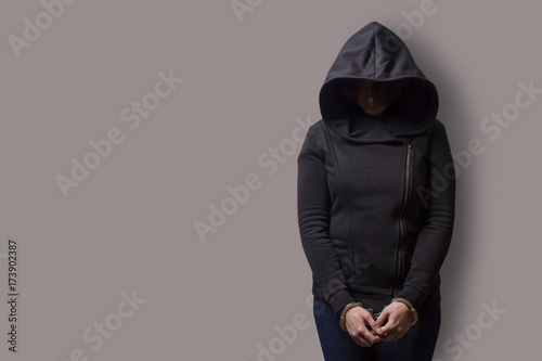 front view of a girl in a black hood with handcuffed hands isolated on a gray