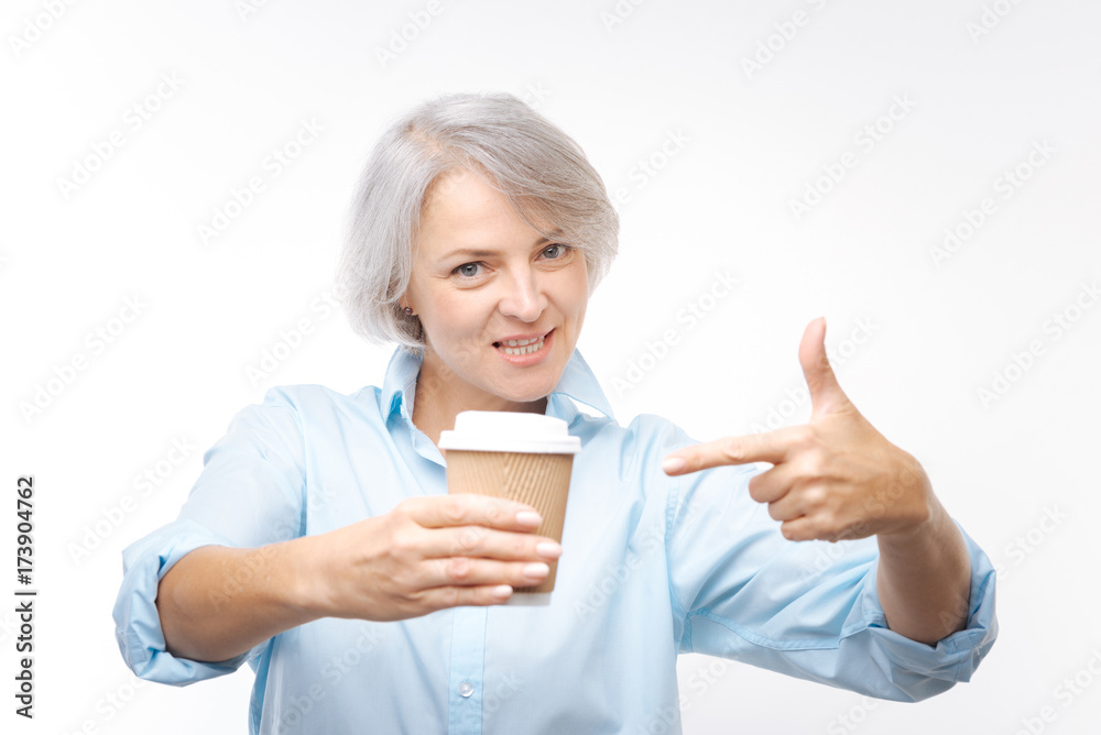 Smiling woman pointing at cup of coffee in her hand Smiling woman pointing at cup of coffee in her hand
