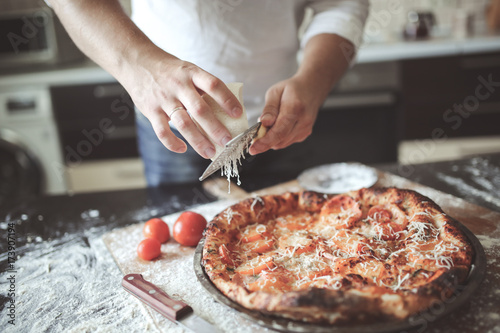 male hands rubbed cheese grated on pizza in home photo