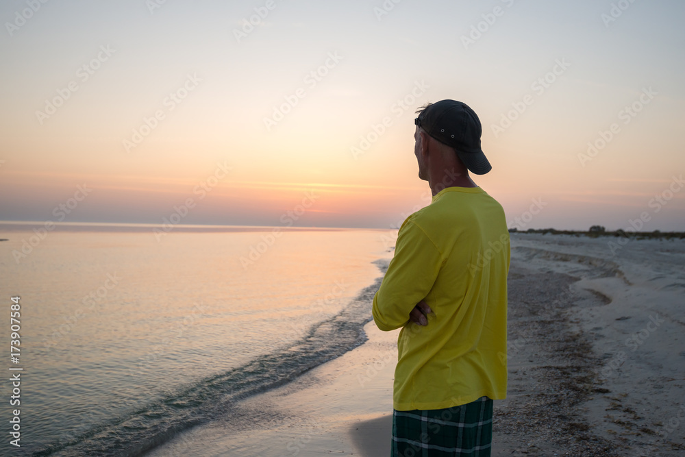 Man traveler is standing alone in a surf line and admiring sunset