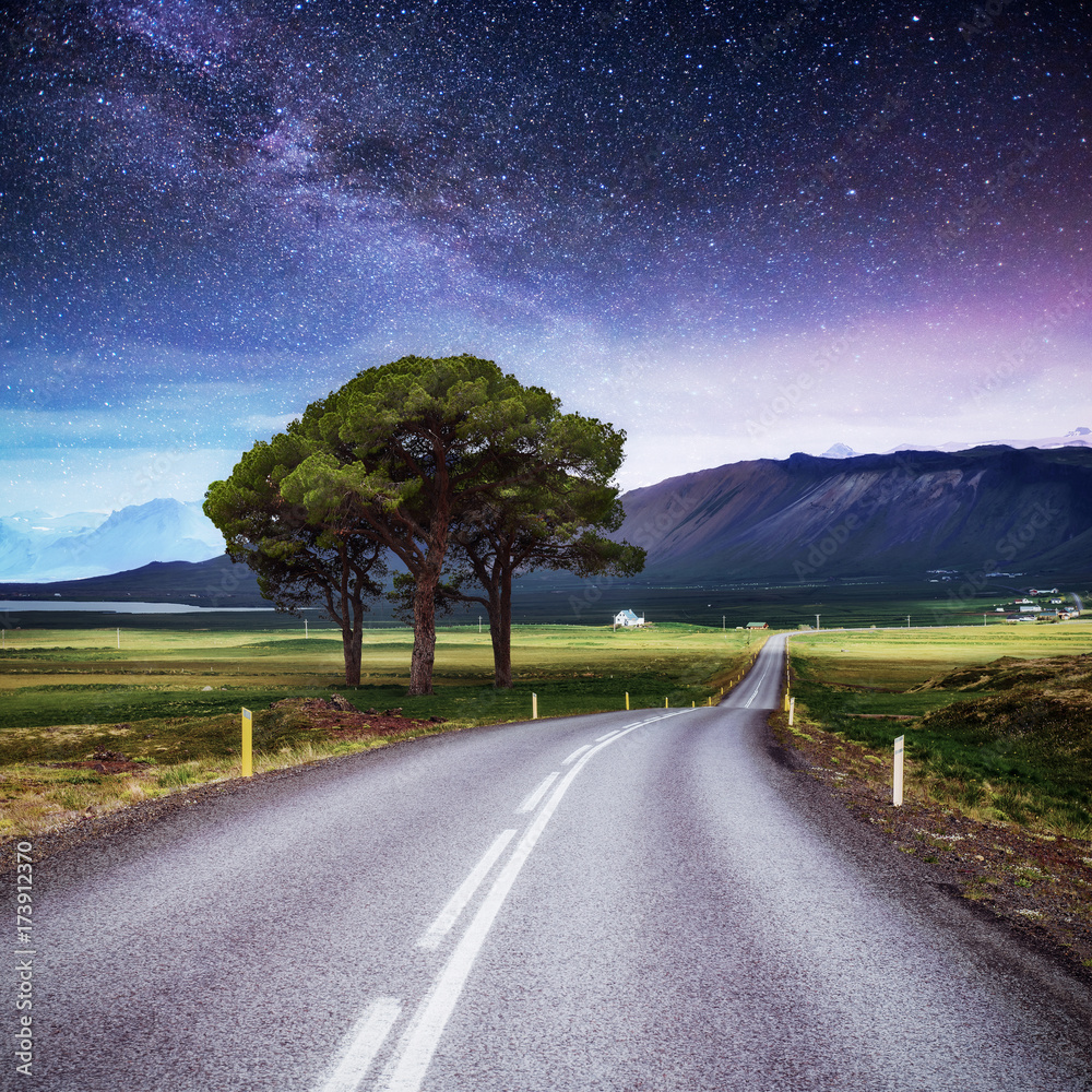 Asphalt road and lonely tree under a starry night sky and the Milky Way ...