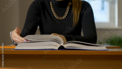 Women's hands leafing through a book. Woman sitting at the table leafing through the book