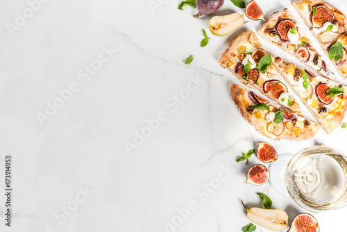Autumn baking recipes. Sweet pie pizza or fruit focaccia with figs, pears, grapes, cream cheese, walnuts and mint. With white wine glass, on white marble background, copy space top view