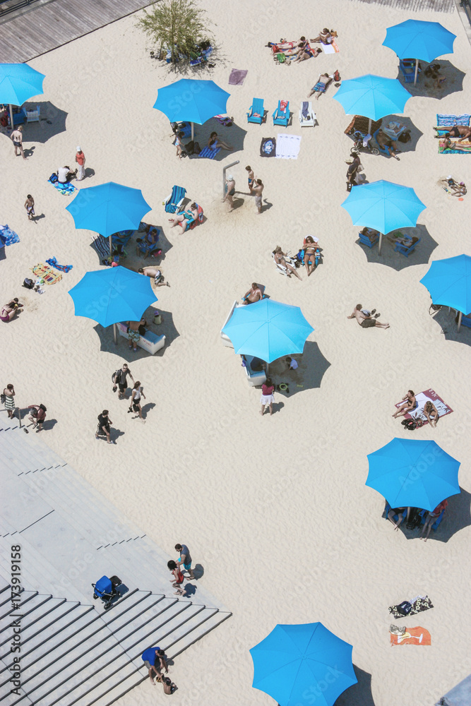 Φωτογραφία people at the beach with blue parasols seen from above
