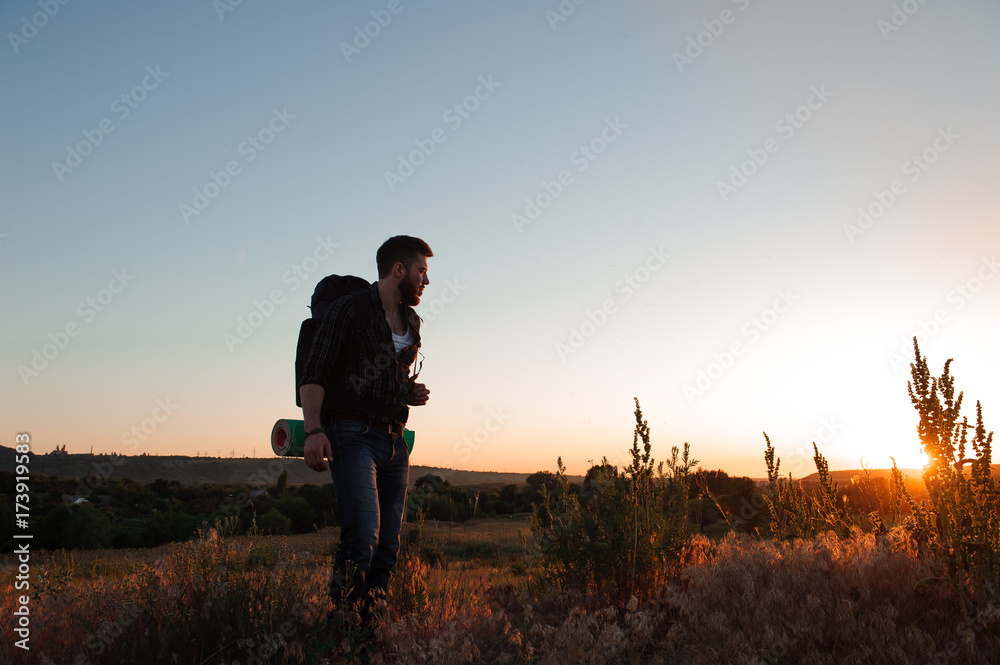 Traveler with backpack standing on a rock and enjoying sunset