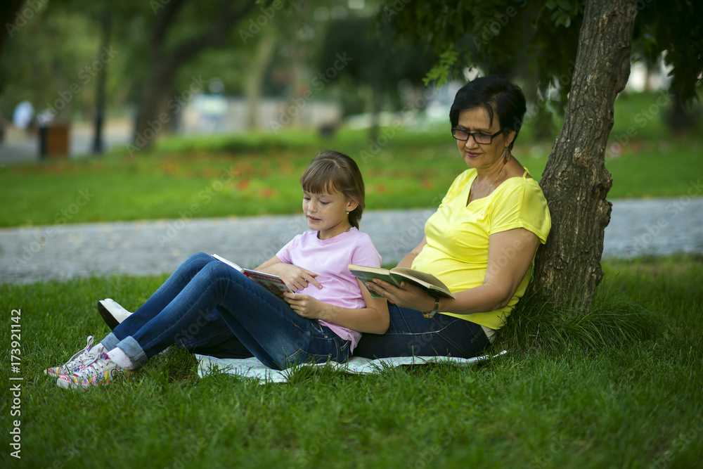 Grandmother and granddaughter reading books sitting on grass in park Grandmother and granddaughter reading books sitting on grass in park