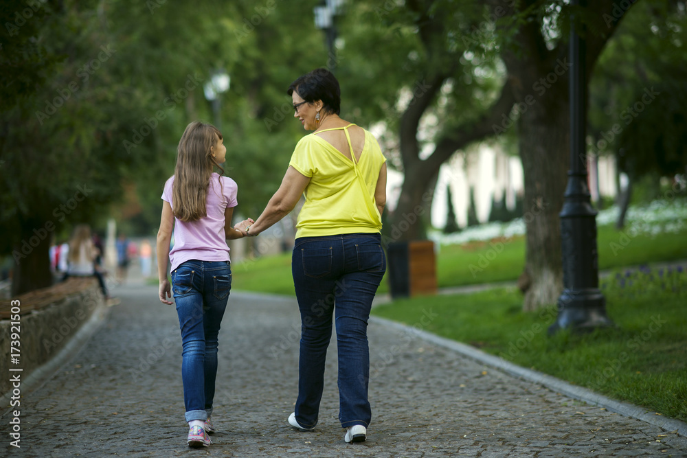 Grandmother and granddaughter are walking in the park to hold hands from the back