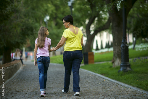 Grandmother and granddaughter are walking in the park to hold hands from the back
