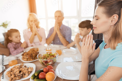 A woman is sitting at a festive table and praying. Against the background  her family sits and also pray