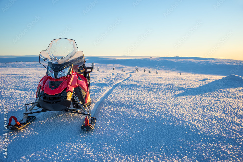 Fototapeta premium Close up photo of a red snowmobile in the snow, snowy landscape, winter adventure in Lapland, near Saariselka, Finland