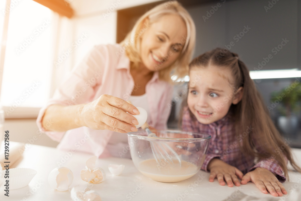 Grandmother drives the egg into the dough. She teaches her granddaughter how to cook a homemade cake Grandmother drives the egg into the dough. She teaches her granddaughter how to cook a homemade cake