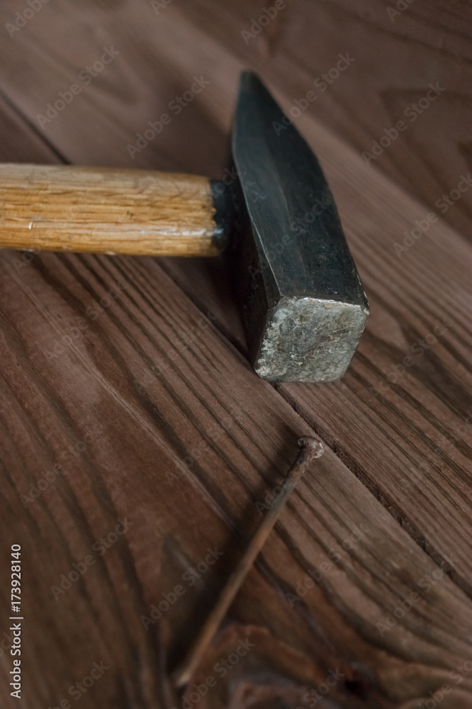Old used hammer, wooden handle, metal head and rusty nail on wooden backdrop