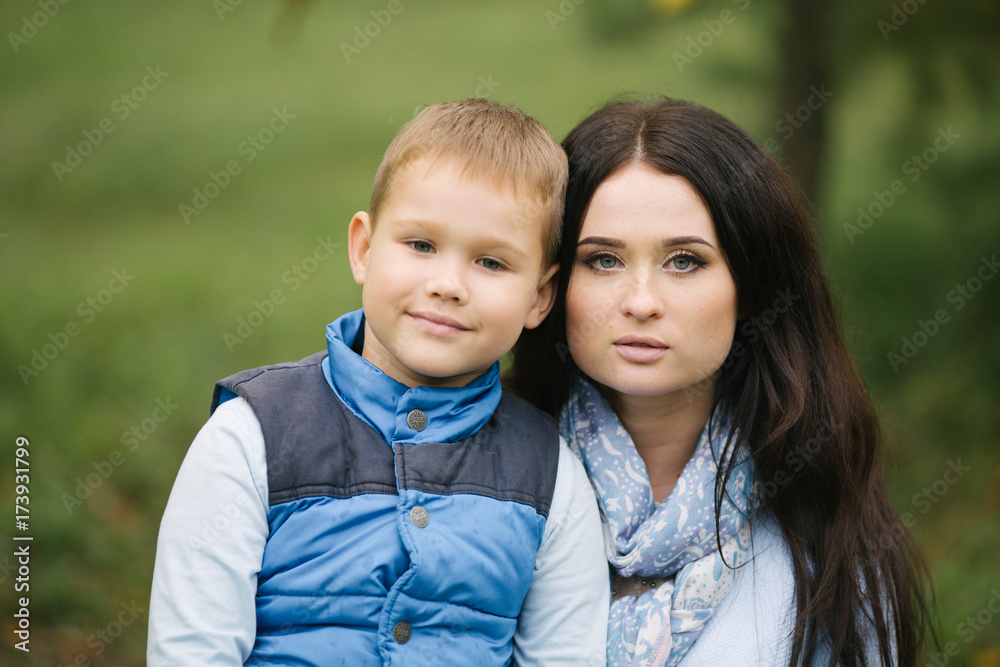 Portrait of a young and cute woman and her son, a child in autumn clothes tilted his head at mom, mom loves her baby and takes care of him Portrait of a young and cute woman and her son, a child in autumn clothes tilted his head at mom, mom loves her baby and takes care of him