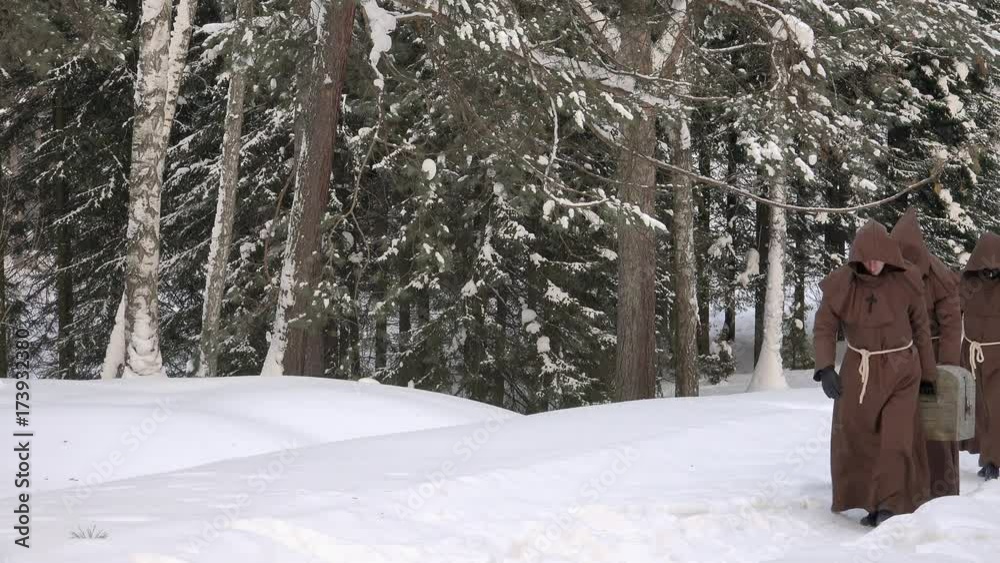 Group of monks pilgrims in hood robe carry old vintage chest box along winter snow trail