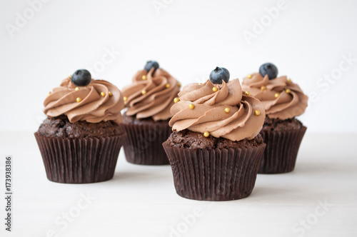 Chocolate cupcakes with whipped chocolate cream, decorated fresh blueberry, gold confectionery sprinkling on white wooden table. Picture for a menu or a confectionery catalog.