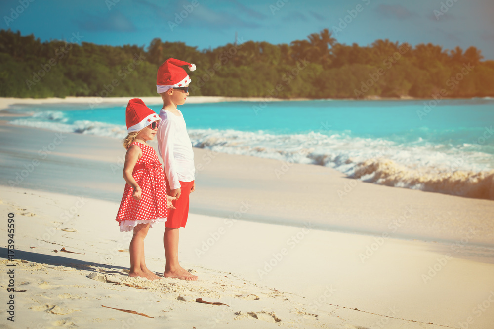 little boy and girl in santa hats having fun on tropical beach at christmas little boy and girl in santa hats having fun on tropical beach at christmas