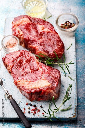 Raw Fresh Marbled Meat Beef Steak and Meat Fork Herbs and Seasonings on a blue Background and a cutting board Rosemary Pepper and Salt Ingredients for Cooking Copy space for Text