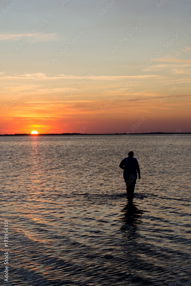 Silhouettes of senior woman walking on the water at the lake at sunset Silhouettes of senior woman walking on the water at the lake at sunset