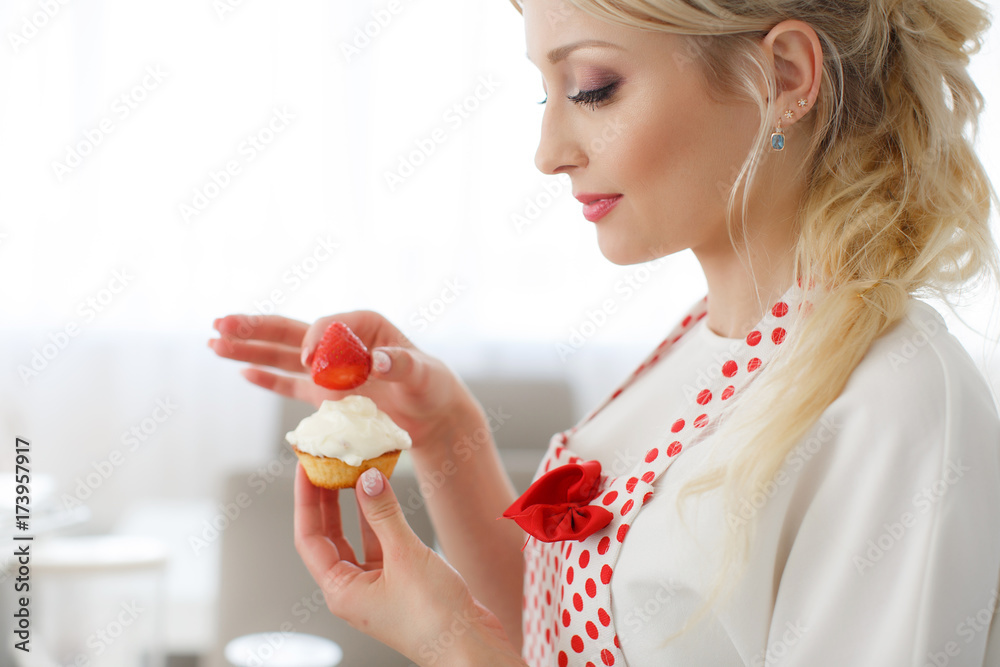 beautiful woman,with long blonde curly hair,dressed in a white t-shirt with short sleeves and white apron for the kitchen with red polka dots,cooks in the kitchen cupcakes with strawberries beautiful woman,with long blonde curly hair,dressed in a white t-shirt with short sleeves and white apron for the kitchen with red polka dots,cooks in the kitchen cupcakes with strawberries